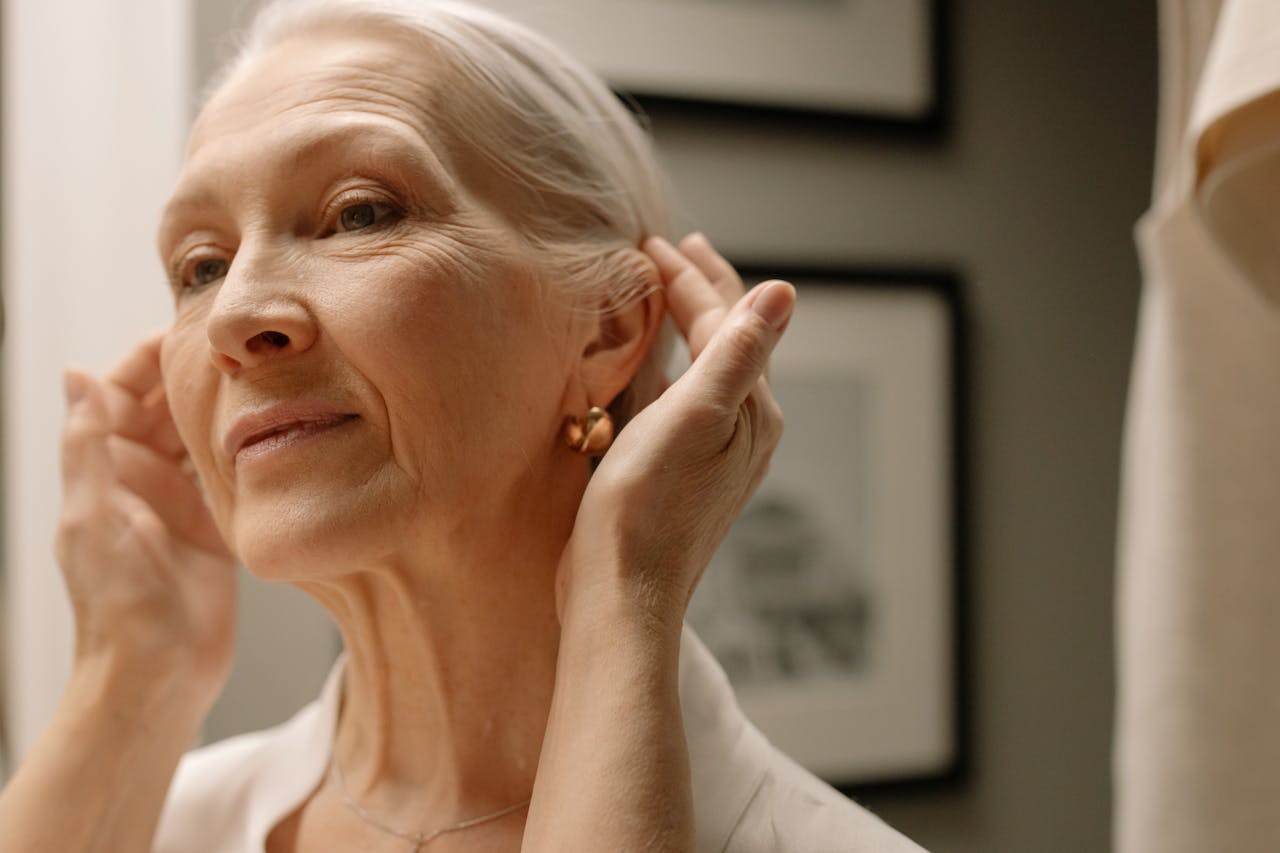 Close-up of an elderly woman adjusting earrings in front of a mirror.