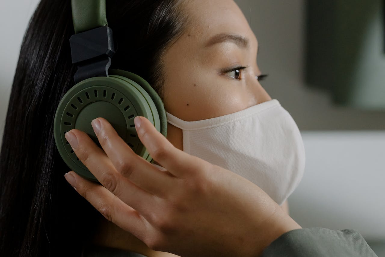 why-choose-us-01 Close-up of a woman wearing a face mask and headphones, listening to music indoors.