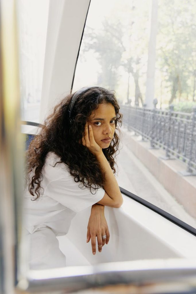 Thoughtful young woman with curly hair and headphones, enjoying a tram ride in the city.