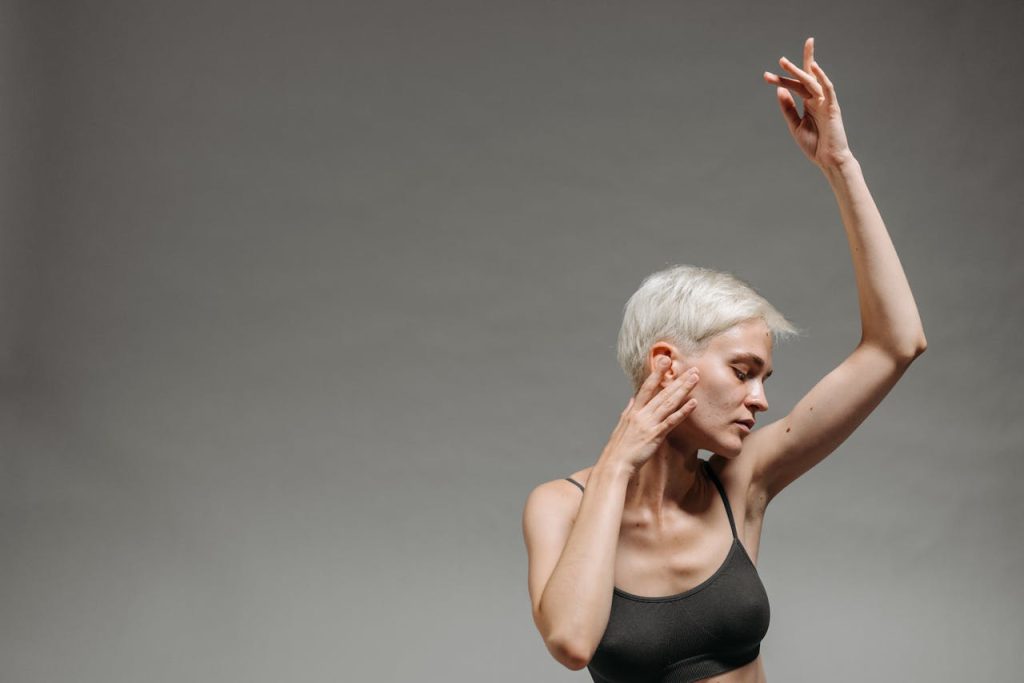 Elegant pose of a woman with short hair in a bralette against a neutral background.